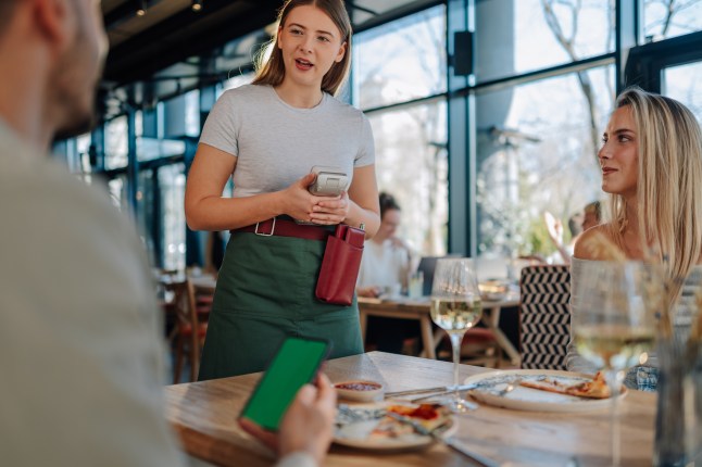 Waitress holding pos terminal assisting customers paying bill in restaurant